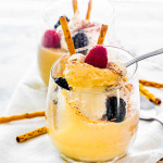 a spoon taking a scoop of homemade vanilla pudding topped with whipped cream, mixed berries and chocolate sticks