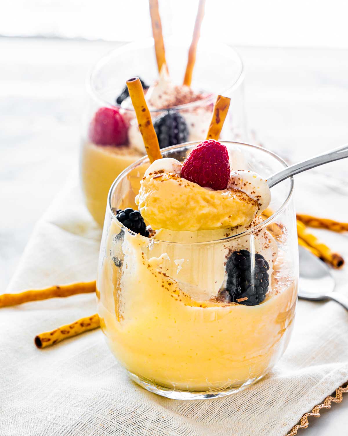 two glasses with homemade vanilla pudding topped with whipped cream and berries