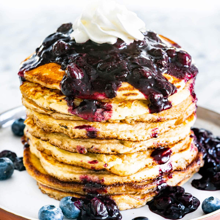 a stack of blueberry buttermilk pancakes topped with blueberry sauce and whipped cream