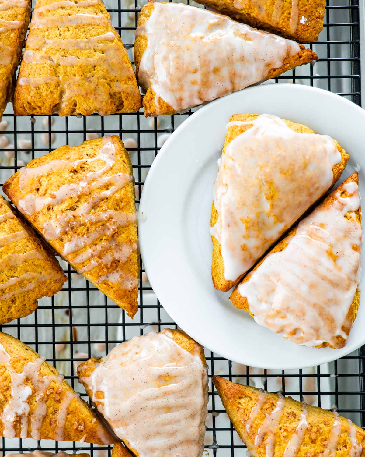 overhead of pumpkin scones on a cooling rack some with glaze on them and a couple on a white plate.