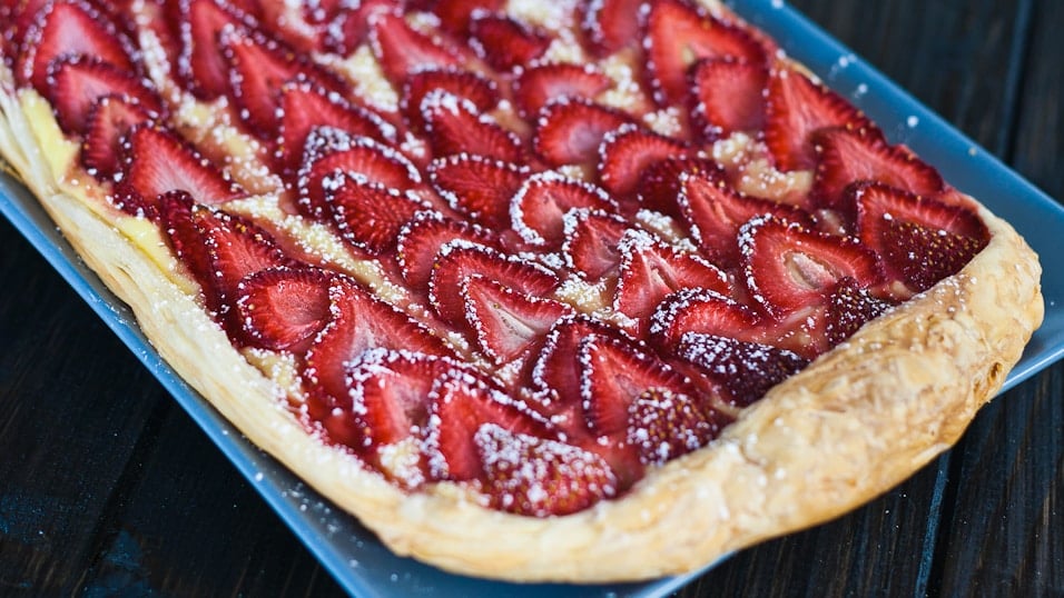Close up shot of strawberry and custard tart dusted with powdered sugar