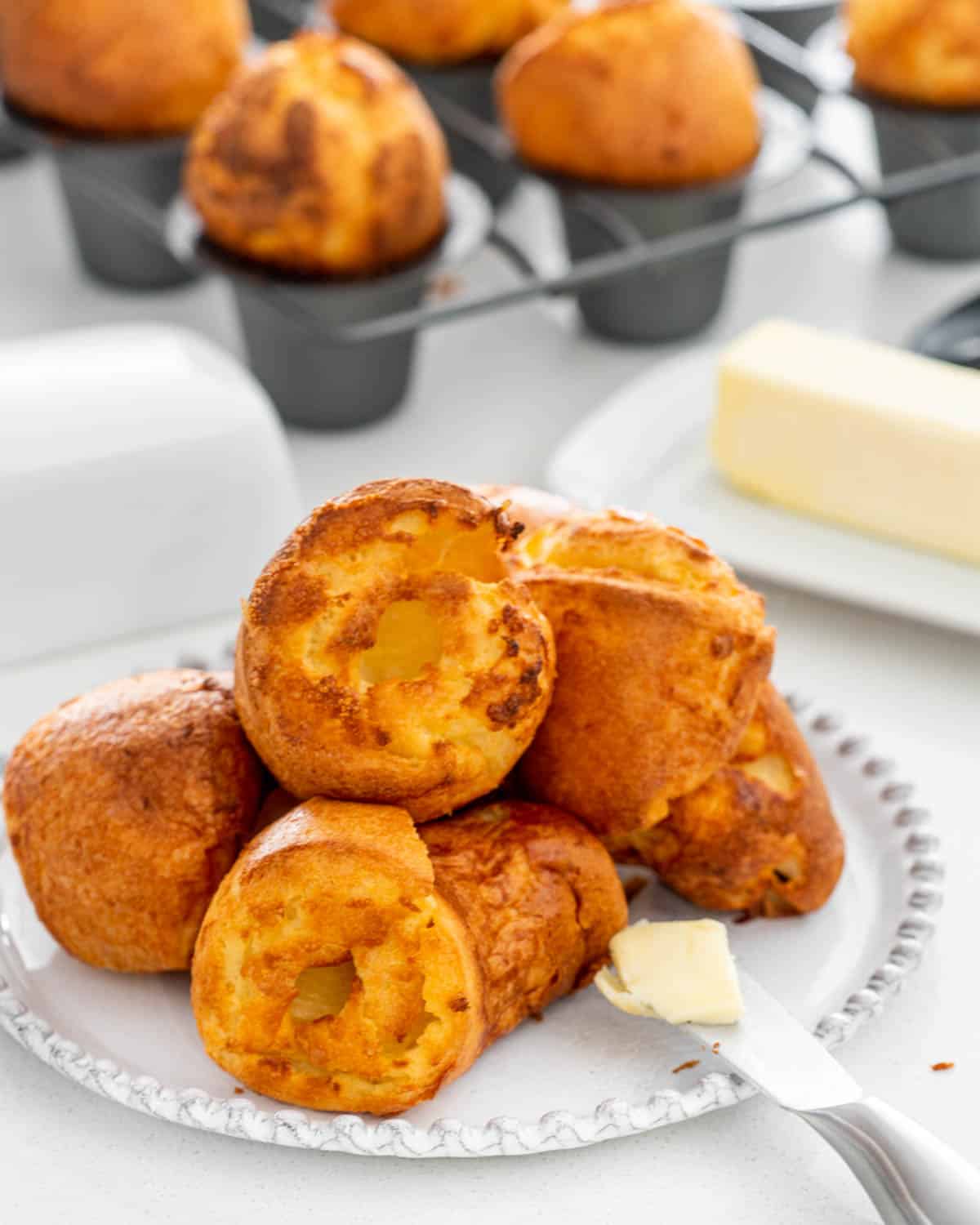 popovers on a white plate with a knife with a pat of butter.