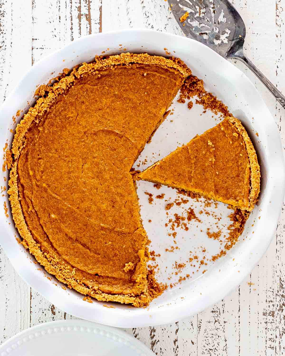 a pie plate with pumpkin pie with graham cracker crust with 2 slices missing.