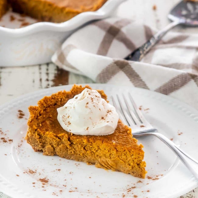 a slice of pumpkin pie with graham cracker crust topped with whipped cream.