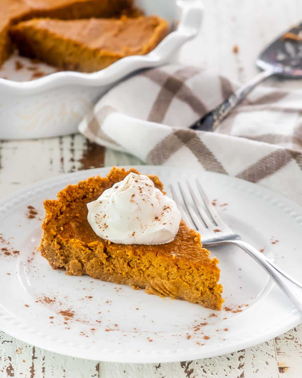 a slice of pumpkin pie with graham cracker crust topped with whipped cream.