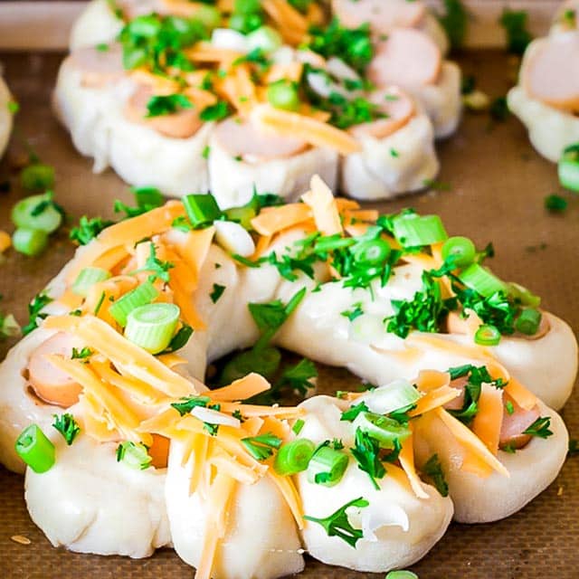 Dough and hot dog pieces topped with cheese, green onion and parsley