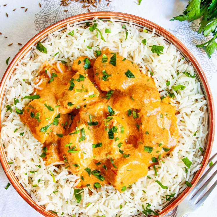 overhead shot of butter chicken on a plate over white rice garnished with parsley