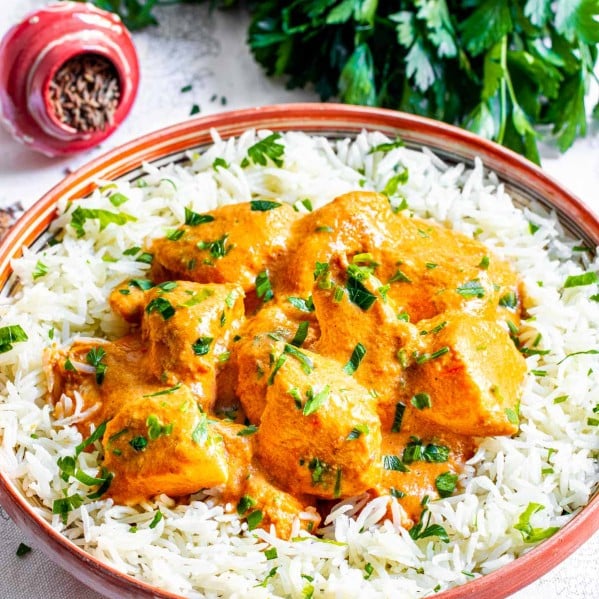 sideview shot of butter chicken on a plate over white rice garnished with parsley
