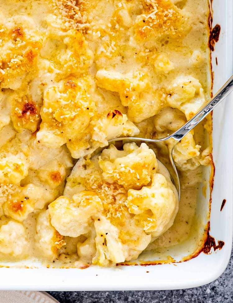 cauliflower au gratin in a baking dish with a serving spoon inside.