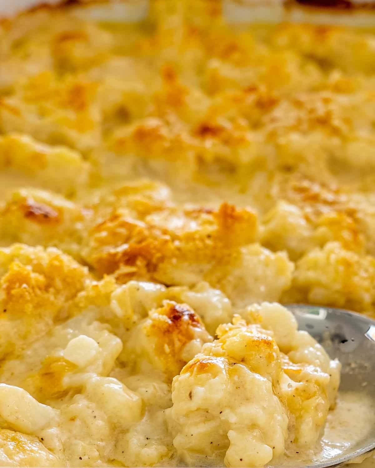 cauliflower au gratin in a baking dish with a serving spoon inside.