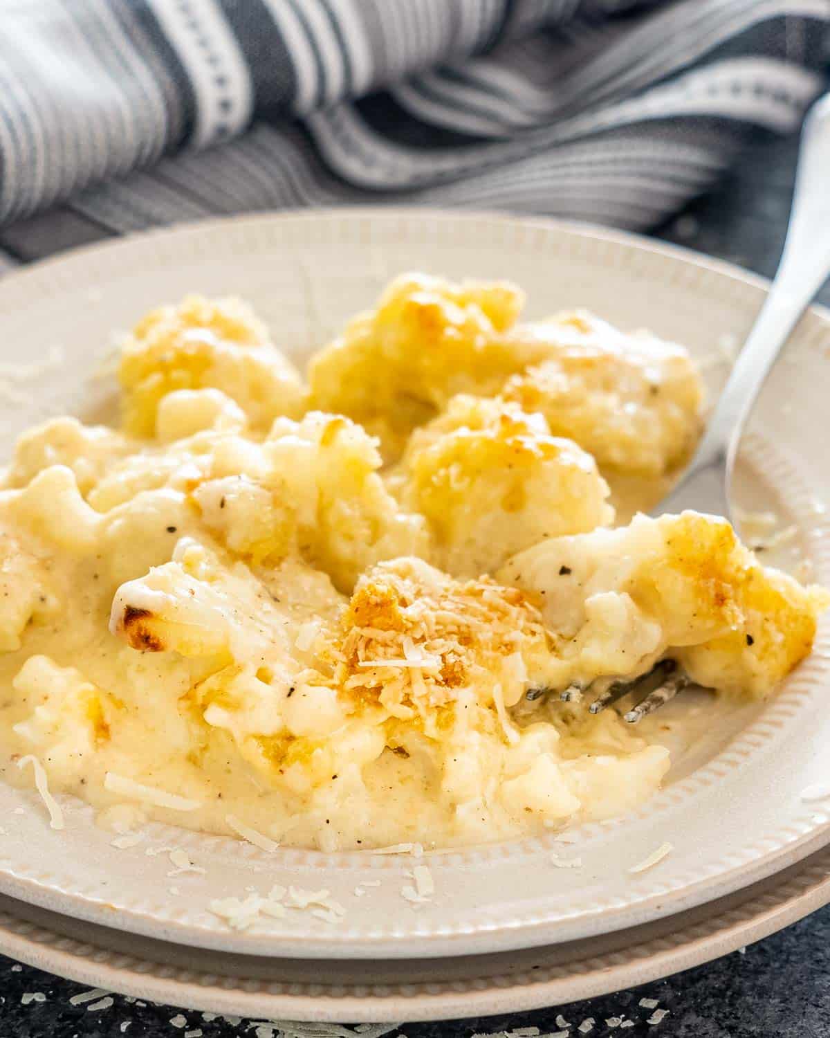 a serving of cauliflower au gratin in a beige plate with a fork inside.