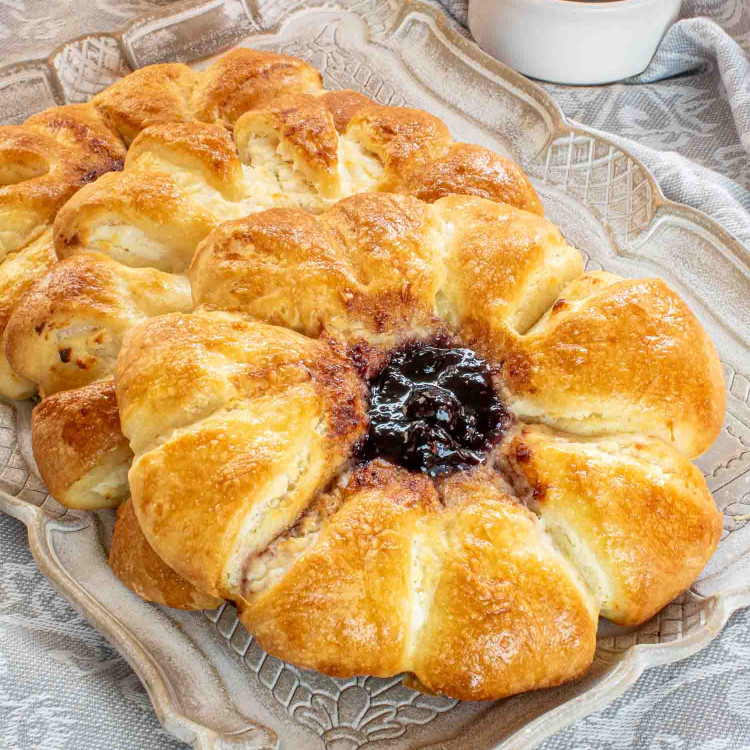 a few cheese danishes with blueberry jam on a serving platter.