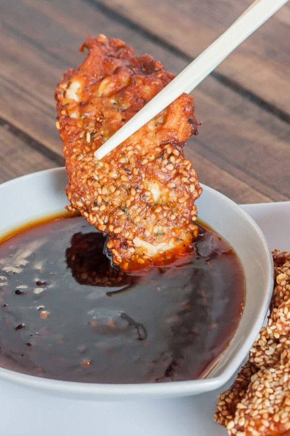 a chopstick dipping a piece of shanghai chicken in sauce