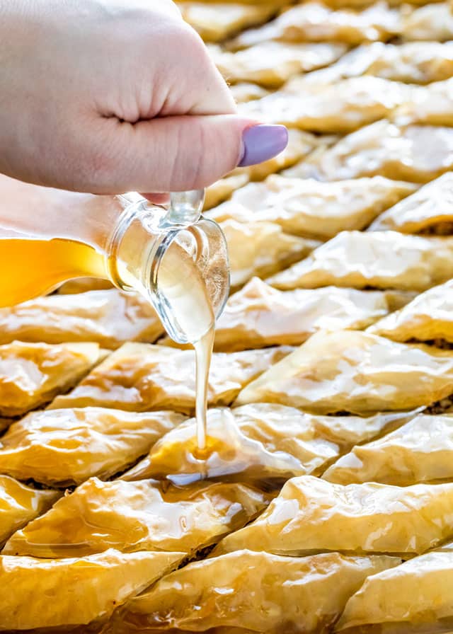 a hand pouring syrup over baklava