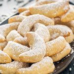 pineapple coconut crescent cookies on a plate dusted with powdered sugar.