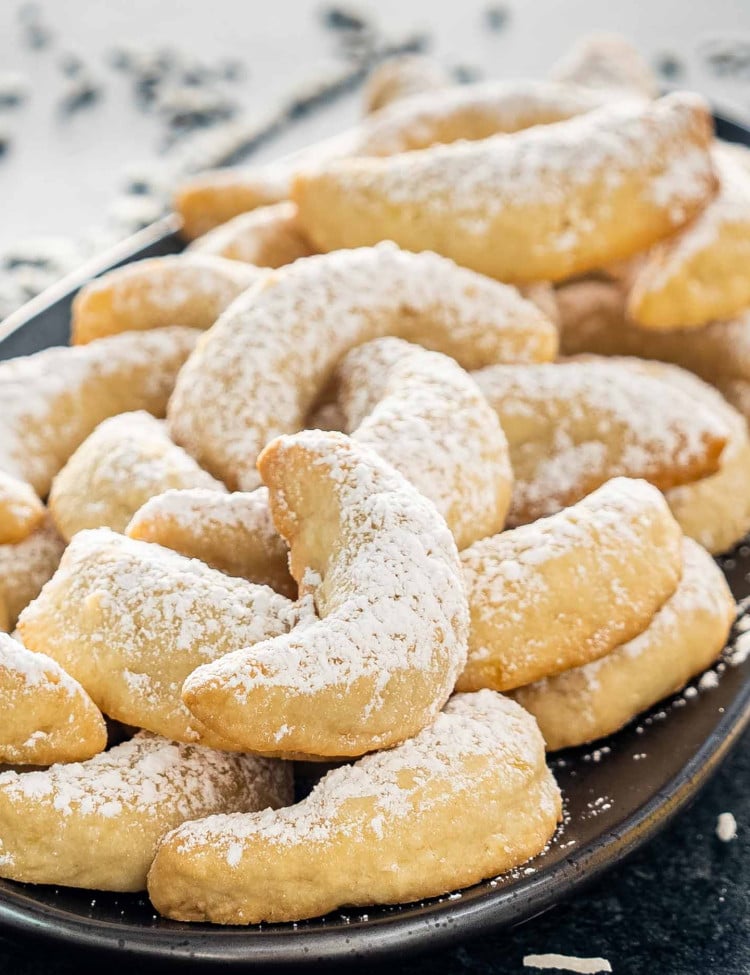 pineapple coconut crescent cookies on a plate dusted with powdered sugar.