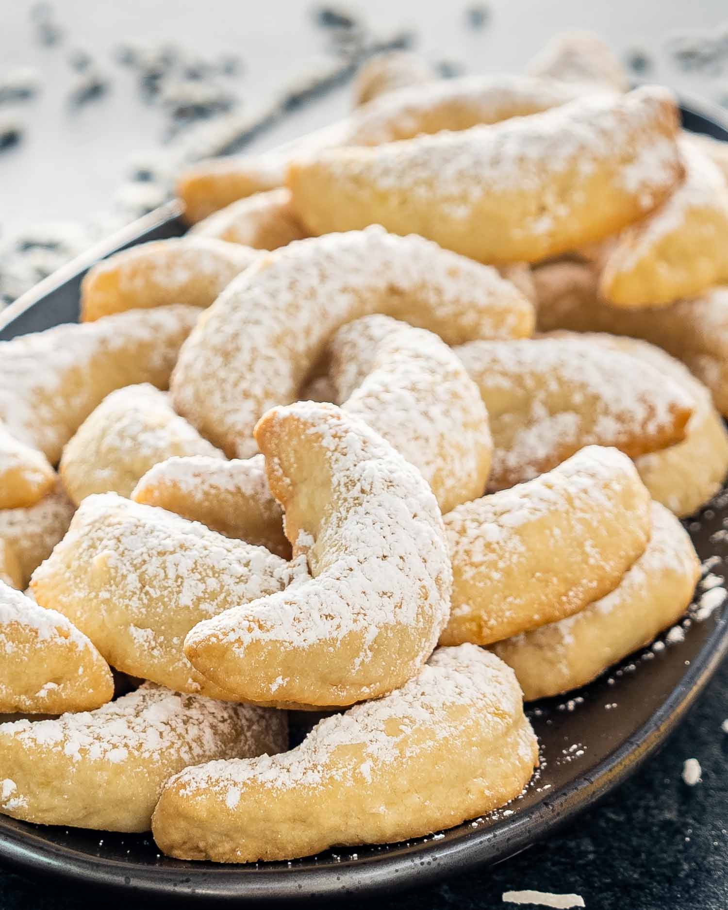 pineapple coconut crescent cookies on a plate dusted with powdered sugar.