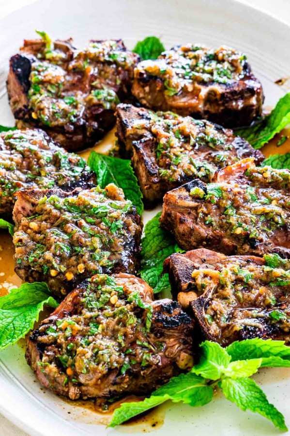 grilled lamb chops with garlic mint sauce on a platter surrounded by mint