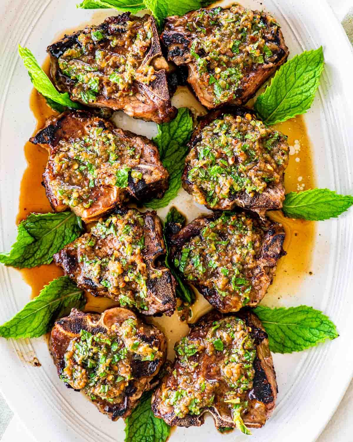 overhead shot of lamb chops on a serving platter with garlic mint sauce and garnished with mint