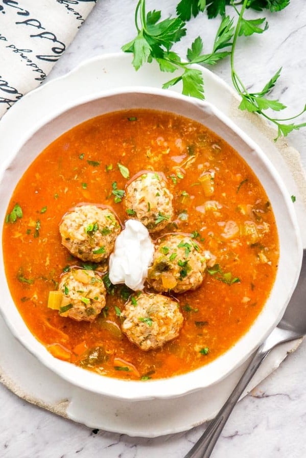 overhead shot of a bowl of romanian meatballs soup topped with a dollop of sour cream
