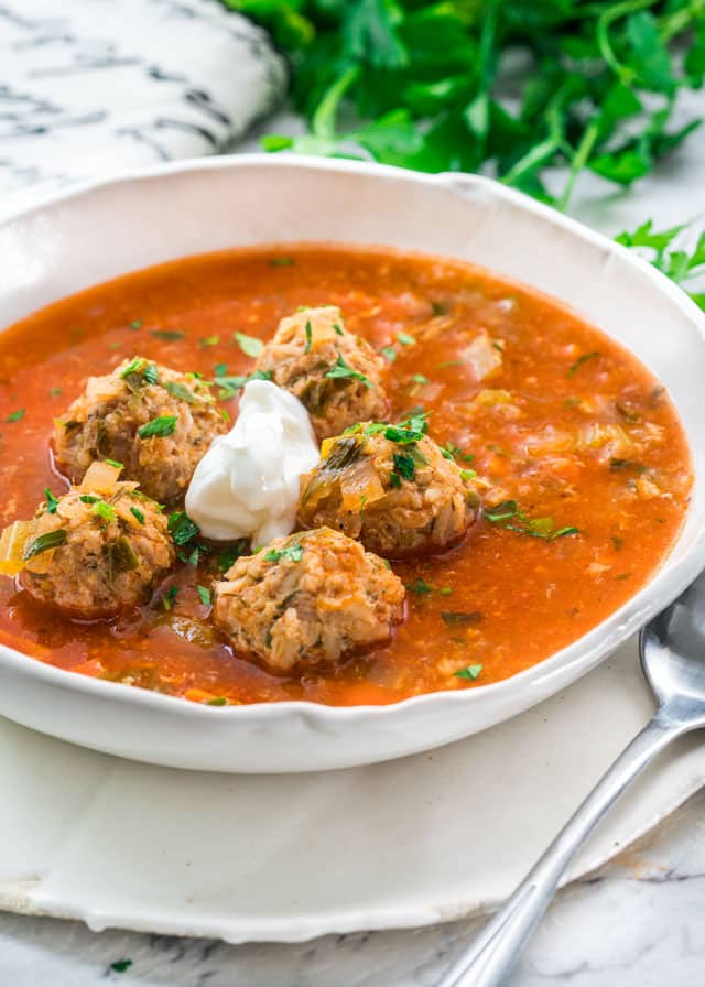 side view shot of a bowl of romanian meatball soup topped with a dollop of sour cream