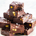 a stack of freshly made nutella fudge pieces on a white plate with the top piece having a bite taken out of it