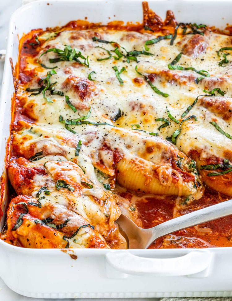 side view shot of stuffed shells in a baking dish with a serving spoon taking a scoop