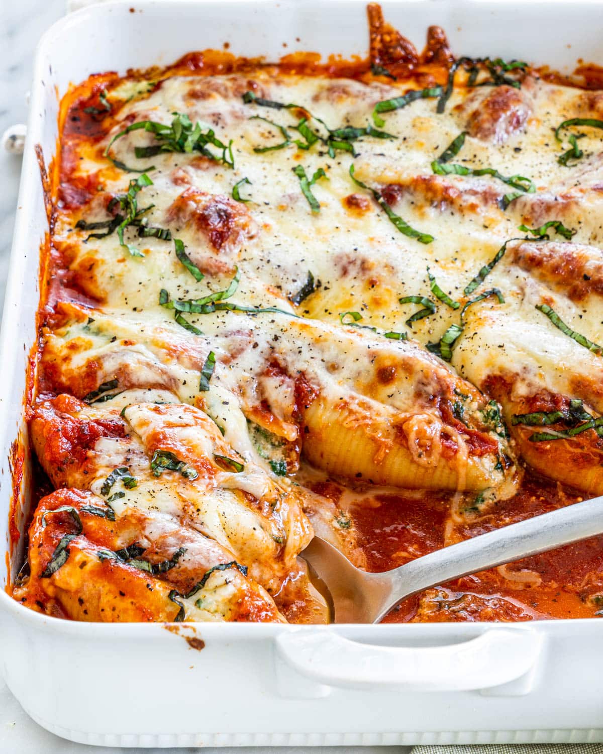 a spoon holding two pasta shells in a casserole dish full of stuffed shells