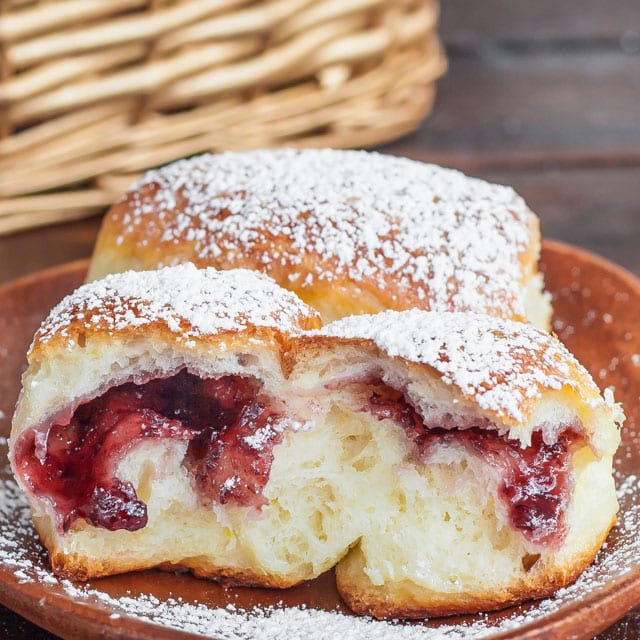 Berry Jam Filled Buns dusted with powdered sugar, one open with berry jam exposed