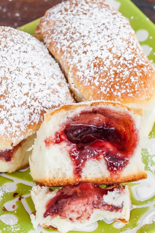 berry jam filled buns on a plate, one ripped open exposing the jam center