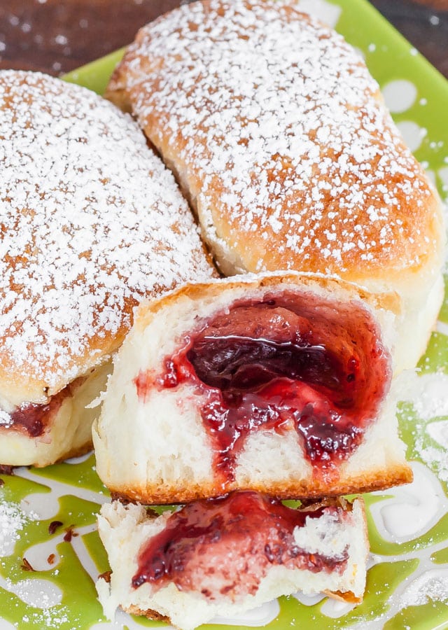 Close up of Berry Jam Filled Buns dusted with powdered sugar, one open with berry jam exposed