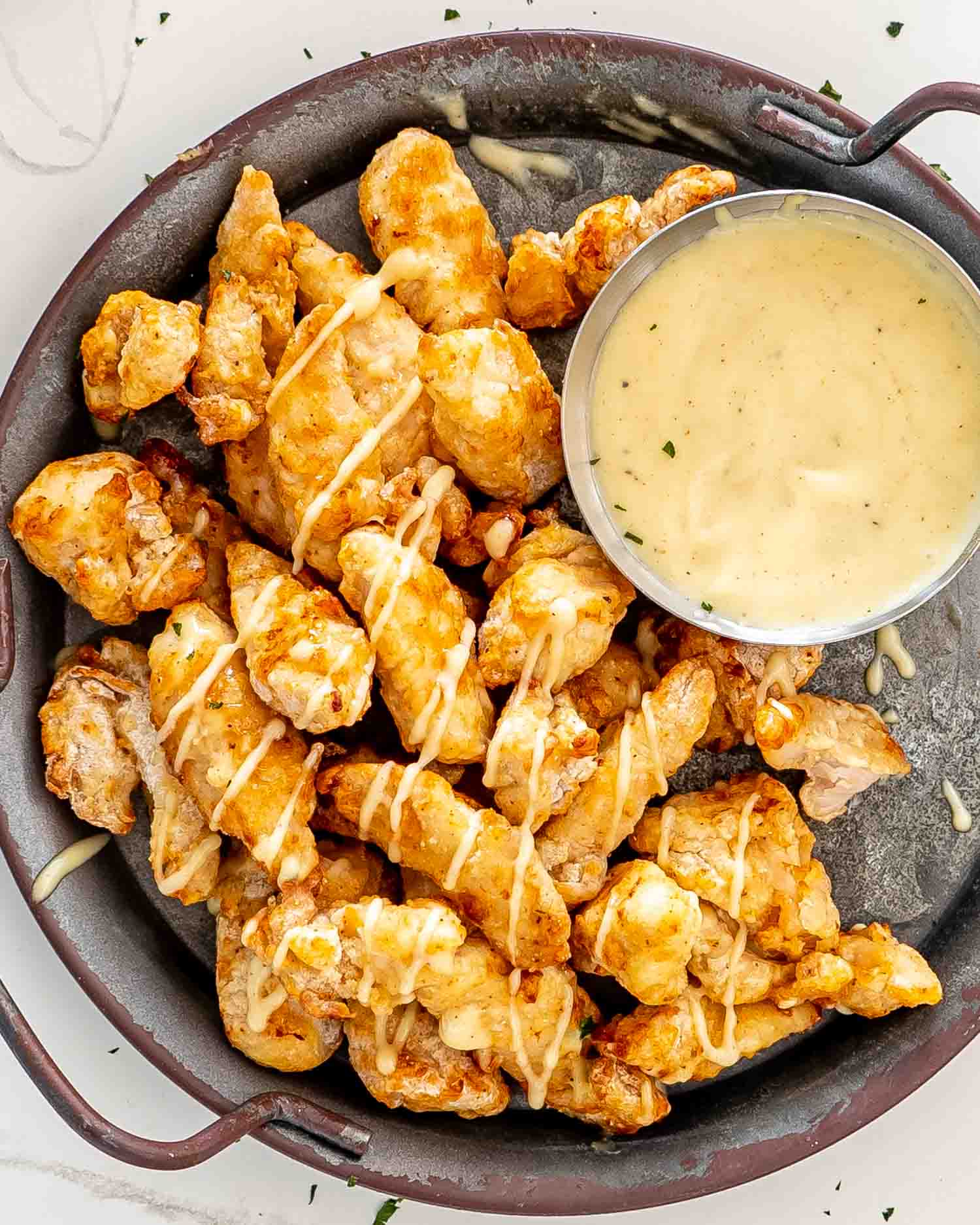 chicken poppers, air fried on a metal plate drizzled with honey mayo sauce.