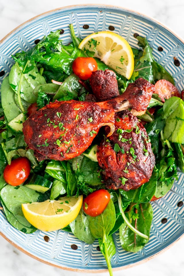 two tandoori chicken drumsticks over a bed of spinach salad