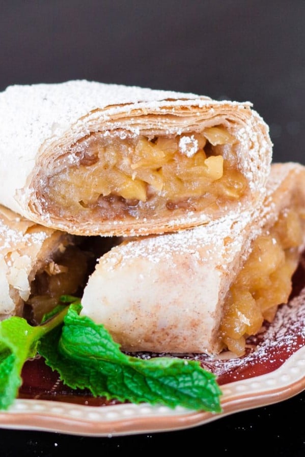 cut in half apple strudel dusted in powdered sugar with filling exposed