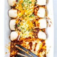 overhead shot of enchiladas in a casserole dish freshly baked with 2 enchiladas missing and a spatula in their place
