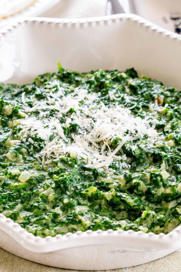 creamed spinach in a white bowl garnished with parmesan cheese.