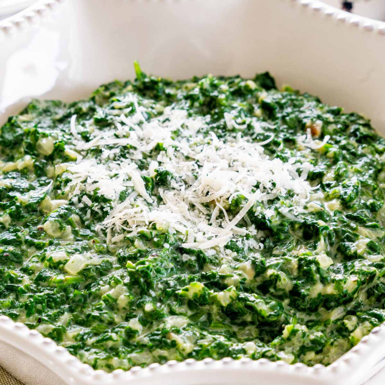 creamed spinach in a white bowl garnished with parmesan cheese.