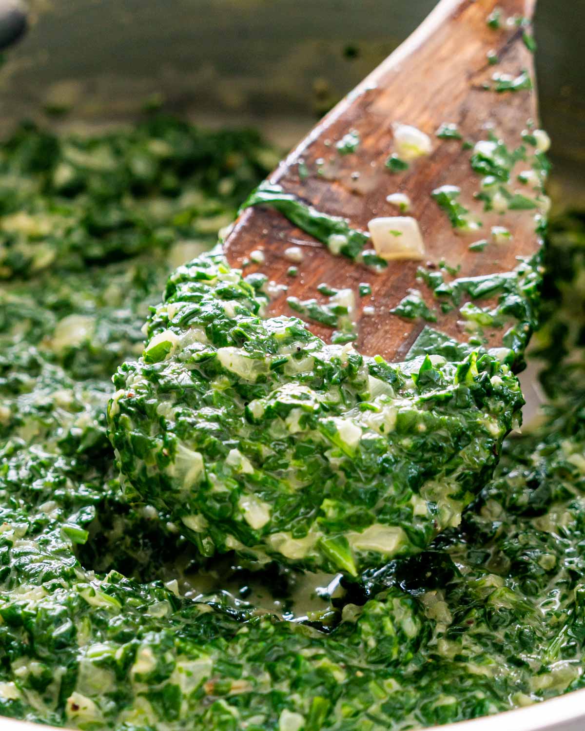 closeup of creamed spinach in a saucepan with a spatula in it.