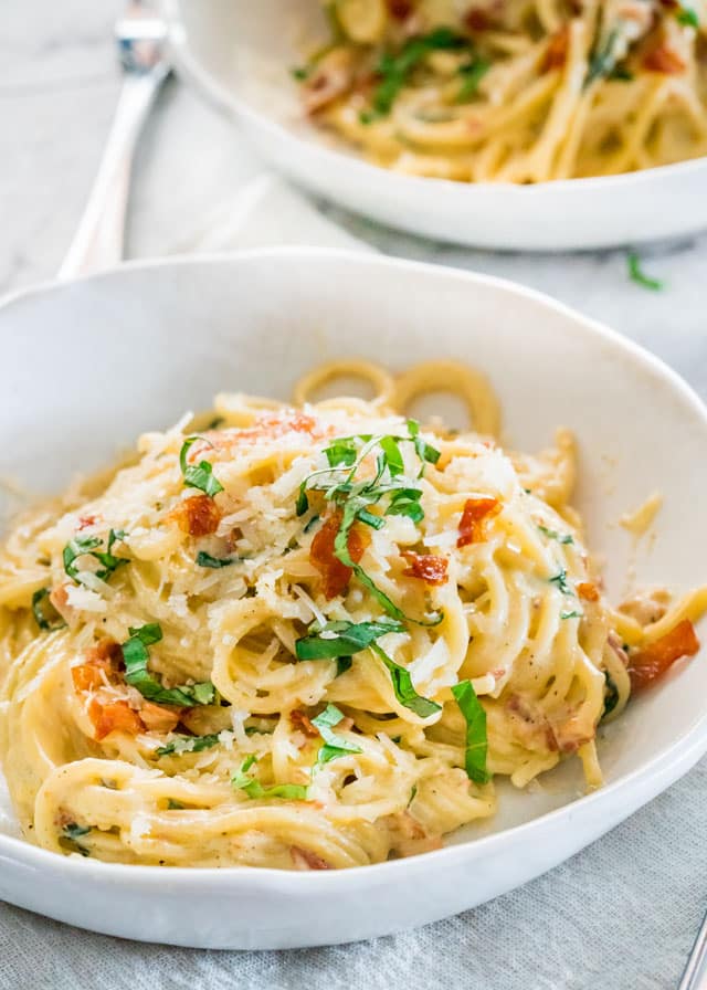 two white plates loaded with creamy carbonara garnished with basil