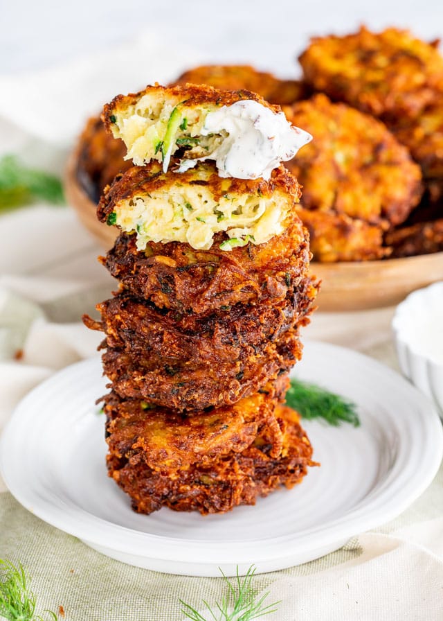 Potato Zucchini Fritters stacked up on a white plate