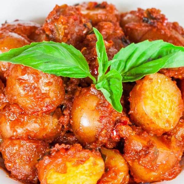 a bowl of potatoes in hot red sauce topped with a sprig of basil