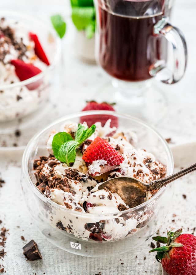 a bowl of chocolaty trifle topped with a strawberry and some mint with a coffee in the background