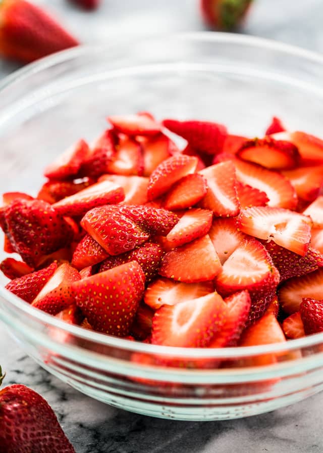 a large clear mixing bowl full of fresh sliced strawberries