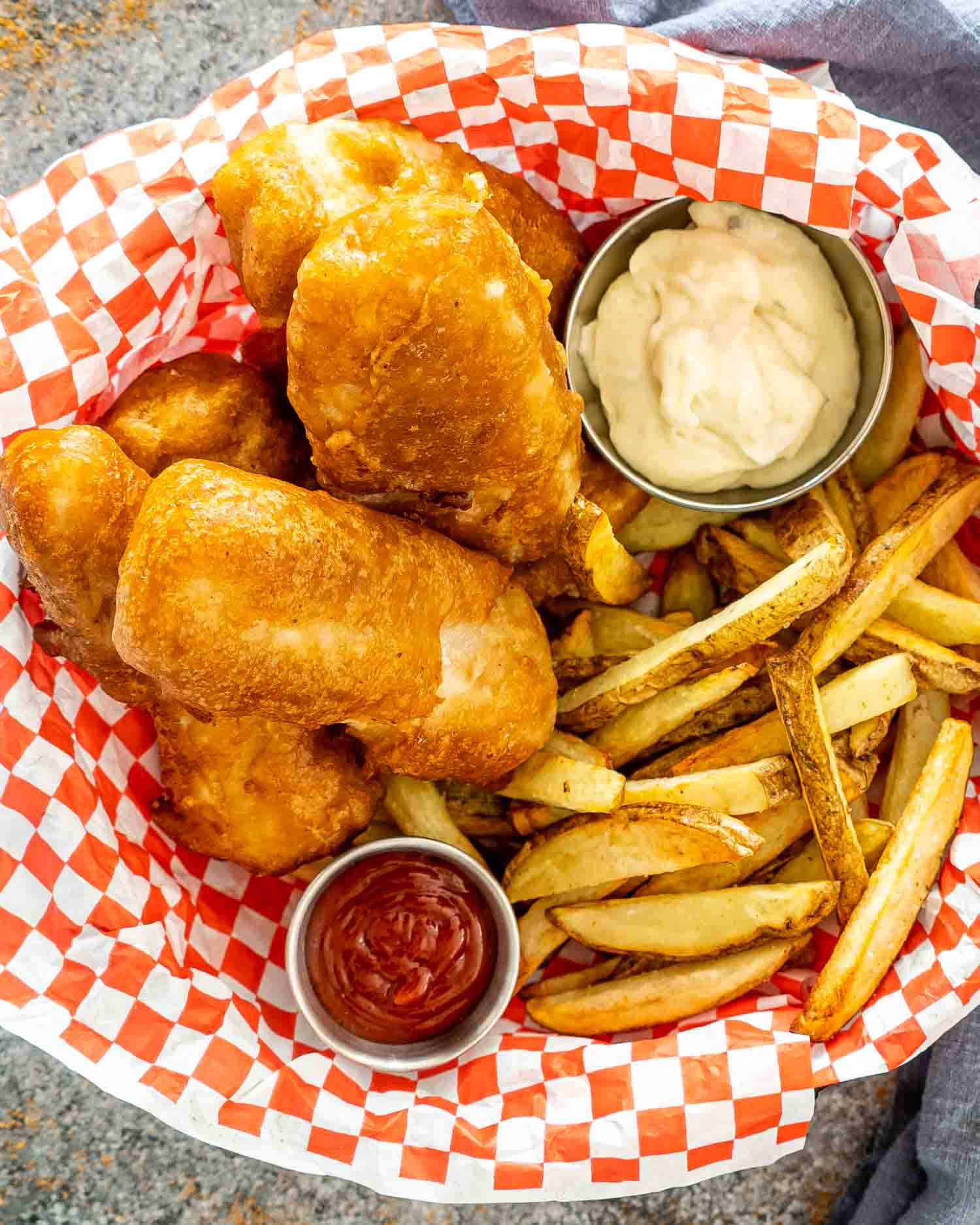 fish and chips in a basket with tartar sauce and ketchup.
