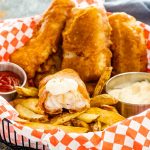fish and chips in a basket with tartar sauce and ketchup.