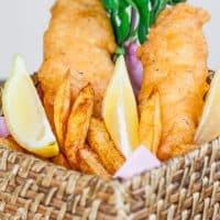 a basket of fish and chips garnished with lemon wedges