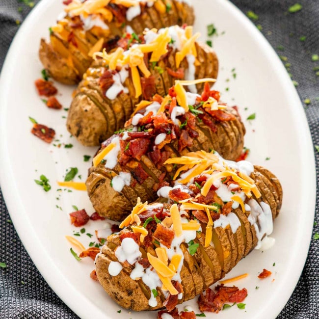 hasselback potatoes on a serving platter garnished with sour cream, bacon and cheese.