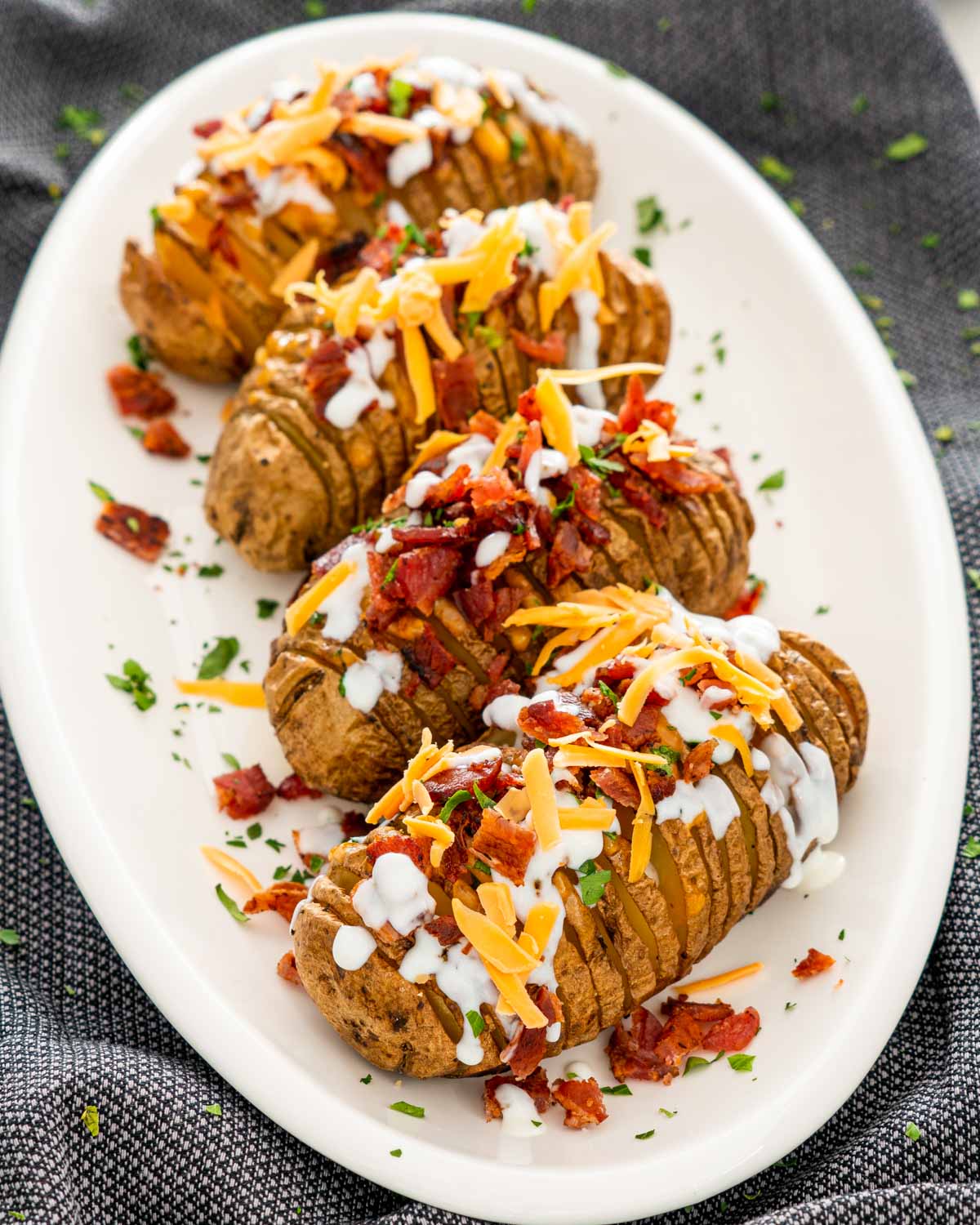 hasselback potatoes on a serving platter garnished with sour cream, bacon and cheese.