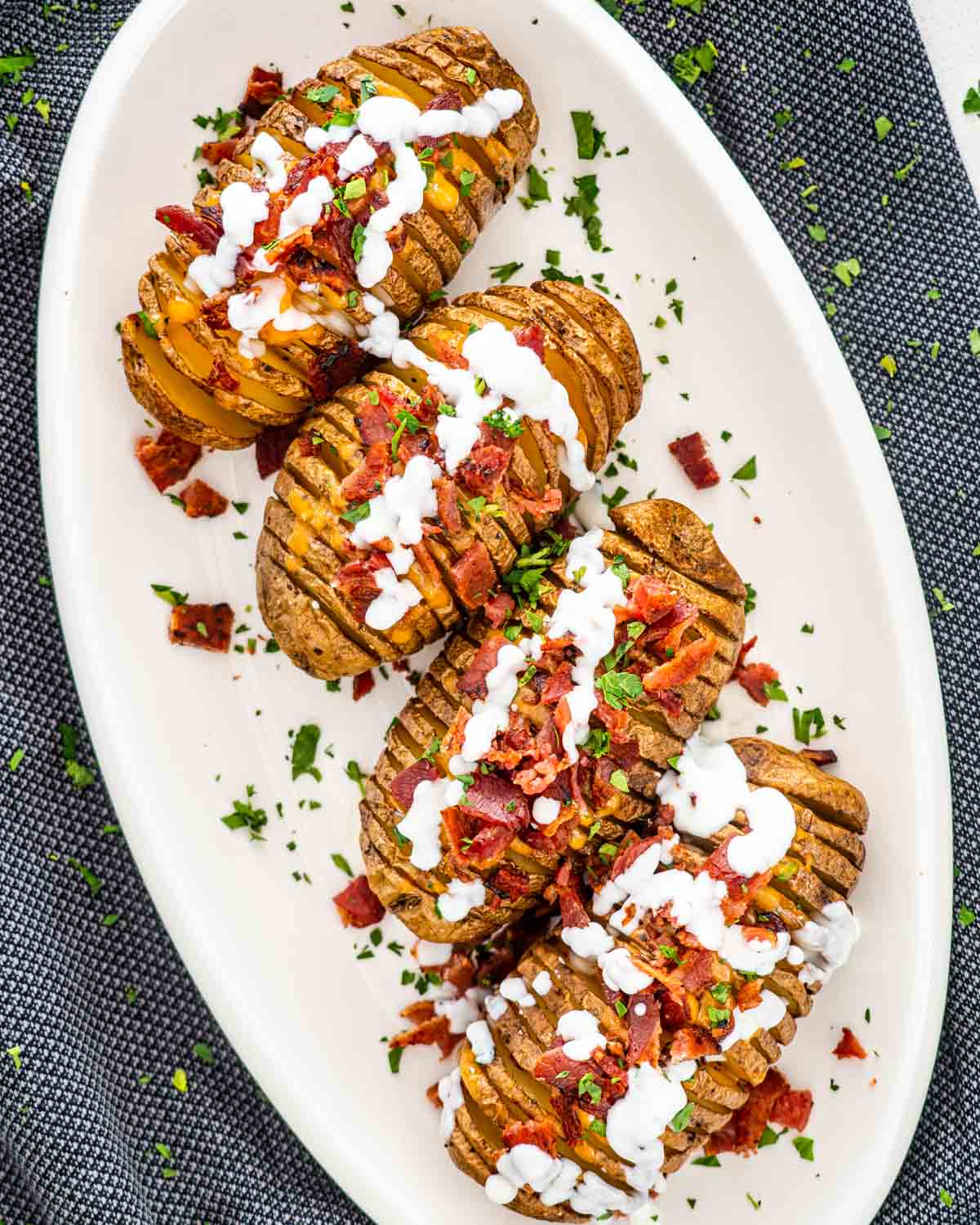 overhead shot of hasselback potatoes on a serving platter garnished with sour cream, bacon and cheese.