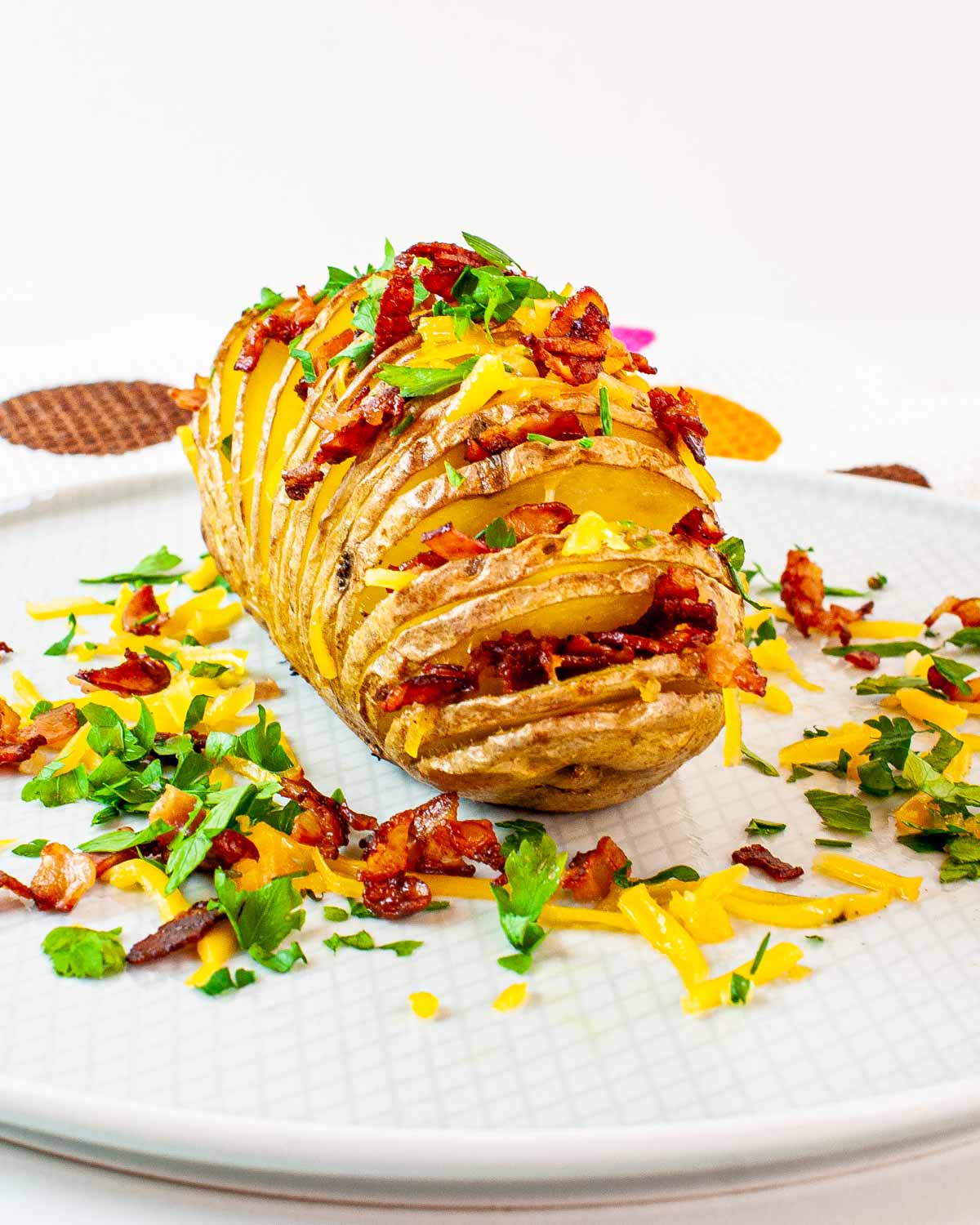 closeup of hasselback potato garnished with bacon, cheese and parsley.